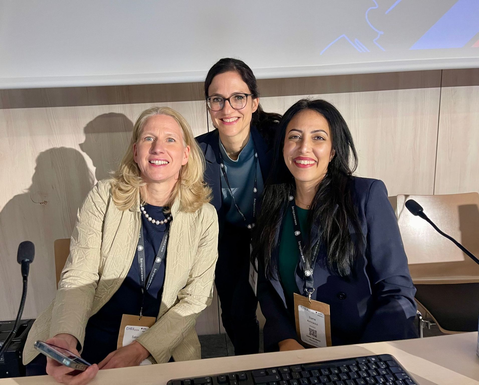 Le Dr Sana Amraoui, souriante, avec deux autres intervenantes à la tribune du congrès EHRA 2026, badges au cou