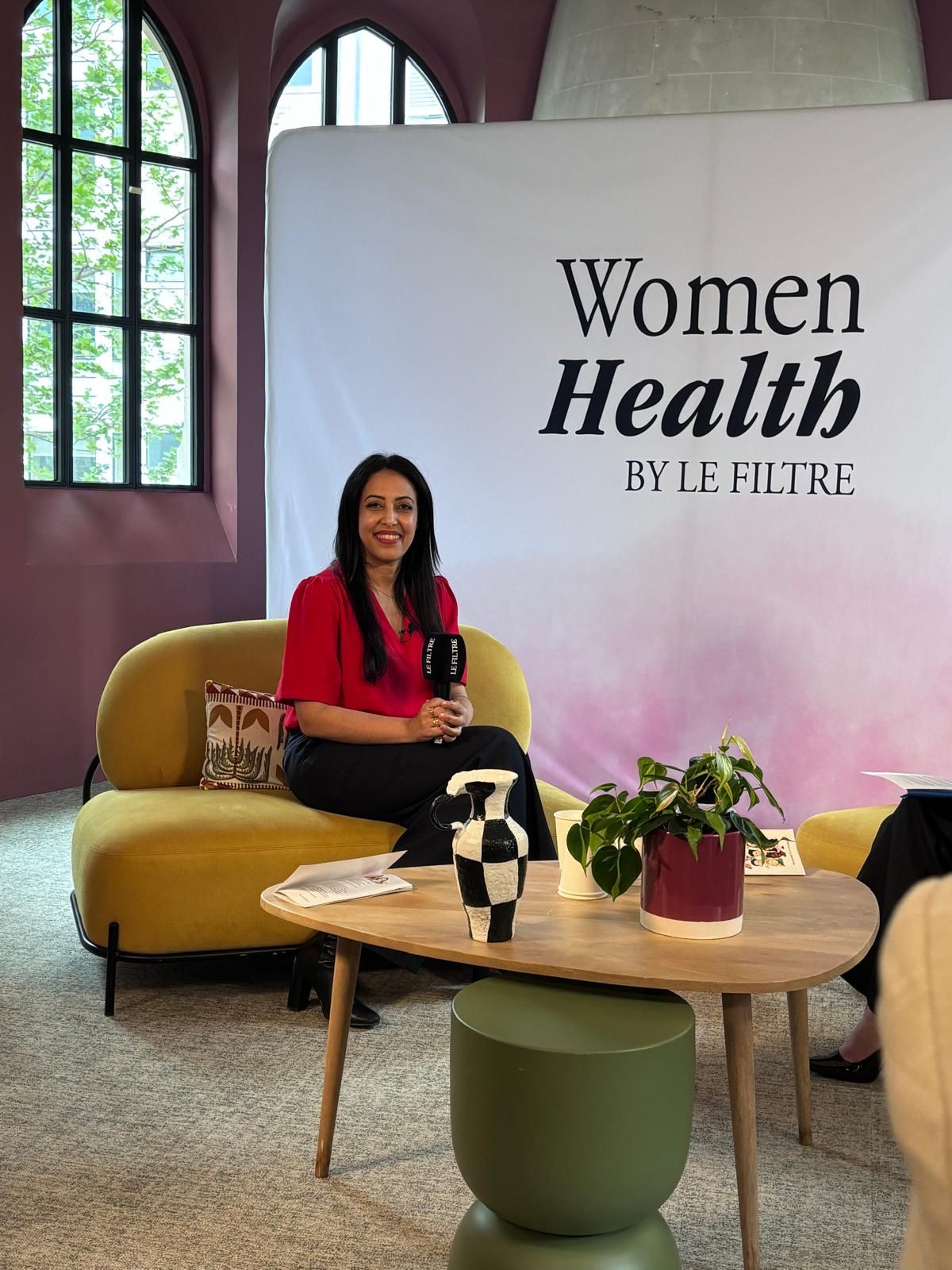 Le Dr Sana Amraoui, en chemisier rouge, micro en main, assise sur le plateau du Women Health Summit by Le Filtre
